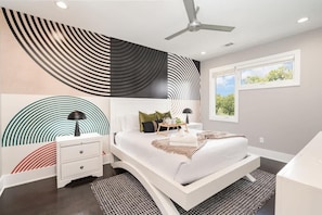 Un dormitorio moderno con cama, mesitas de noche, ventilador de techo y ventana con vistas.