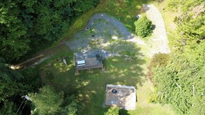 An aerial view of a property with a small wooden structure, a paved area, and dense surrounding foliage.