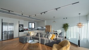 A modern kitchen with stainless steel appliances, a dining area with a grey sofa and yellow cushions, and a wooden floor.