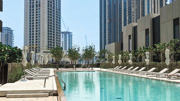Uma piscina com espreguiçadeiras e um deck revestido, cercada por edifícios altos.