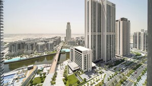 Um edifício residencial alto com design moderno, rodeado por outros edifícios altos, um rio e uma área de parque urbano bem cuidada.