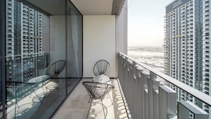 Uma varanda com duas cadeiras, uma mesa e vista para edifícios altos.