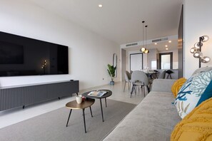 Uma sala de estar moderna com uma televisão de tela plana grande, um sofá, uma mesa de centro e um espaço de jantar com cadeiras e uma mesa.