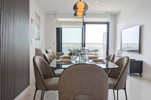 Un espace repas moderne avec une table en verre, six chaises et un luminaire suspendu au design contemporain.