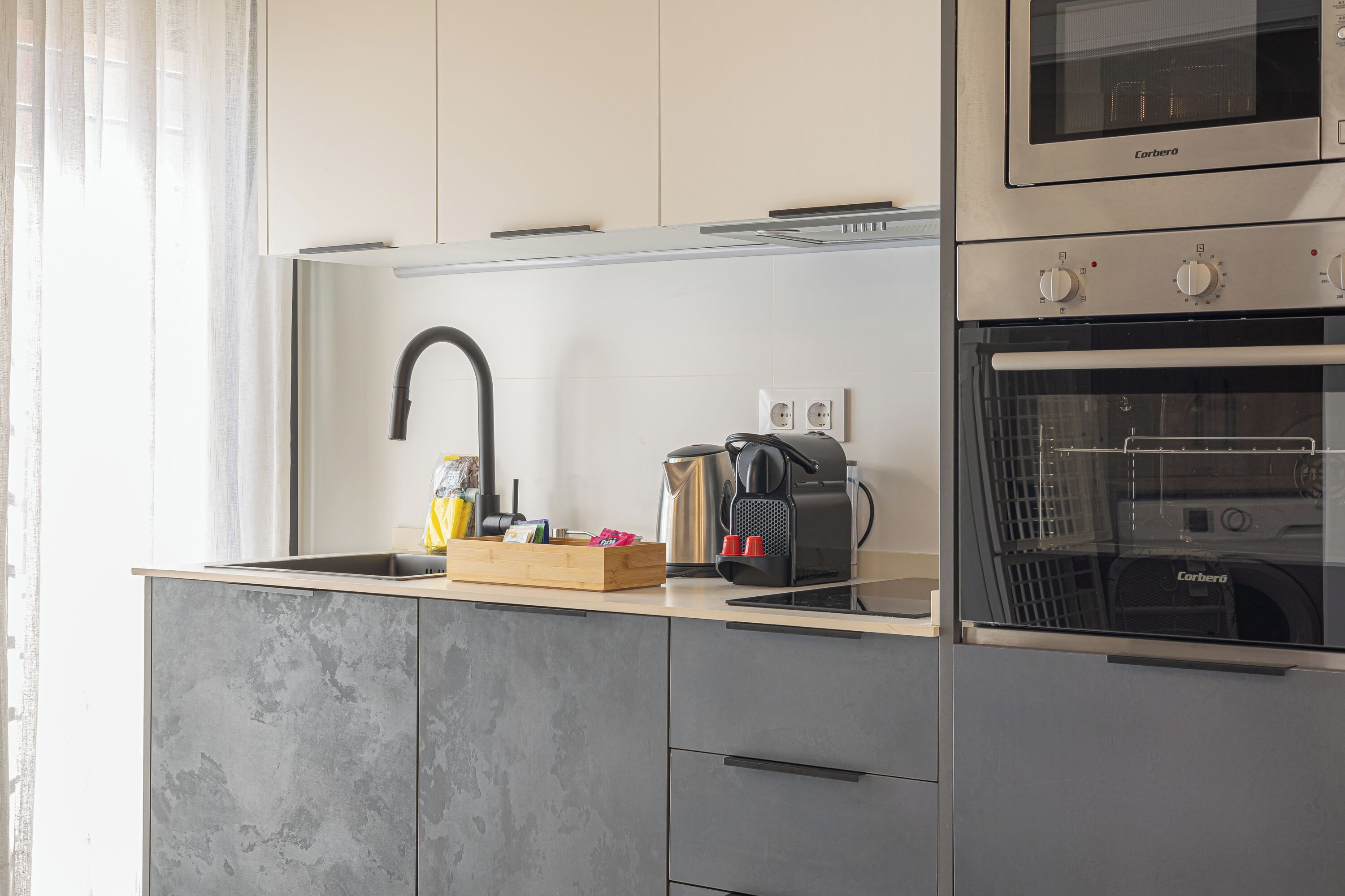 Una cocina moderna con horno empotrado, cafetera y hervidor sobre la encimera.