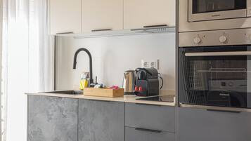Una cocina moderna con horno empotrado, cafetera y hervidor sobre la encimera.