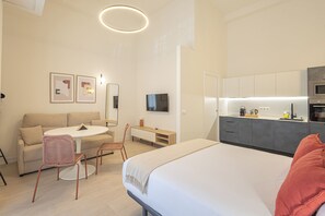 Une chambre d’hôtel moderne comprenant un lit, un coin repas avec une table et des chaises, une kitchenette et un téléviseur fixé au mur.