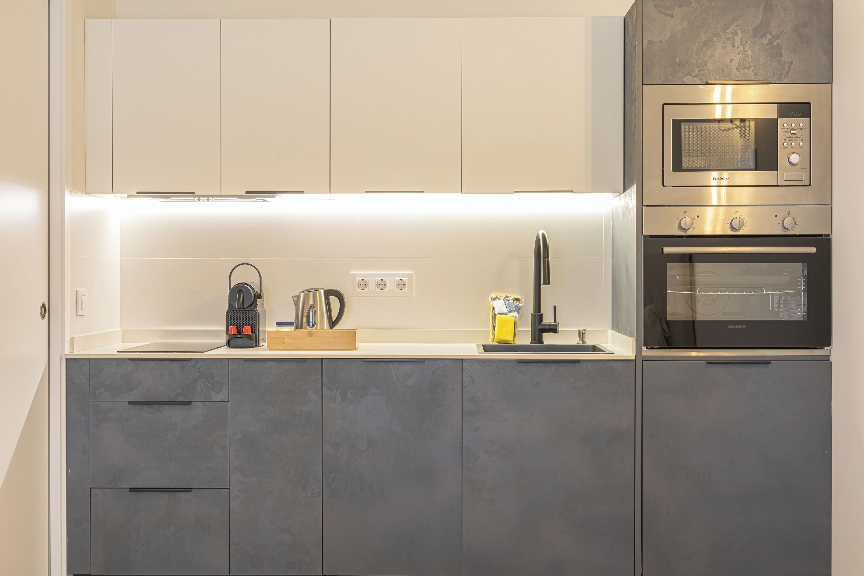 A modern kitchen with grey cabinets, a built-in microwave, and an oven.