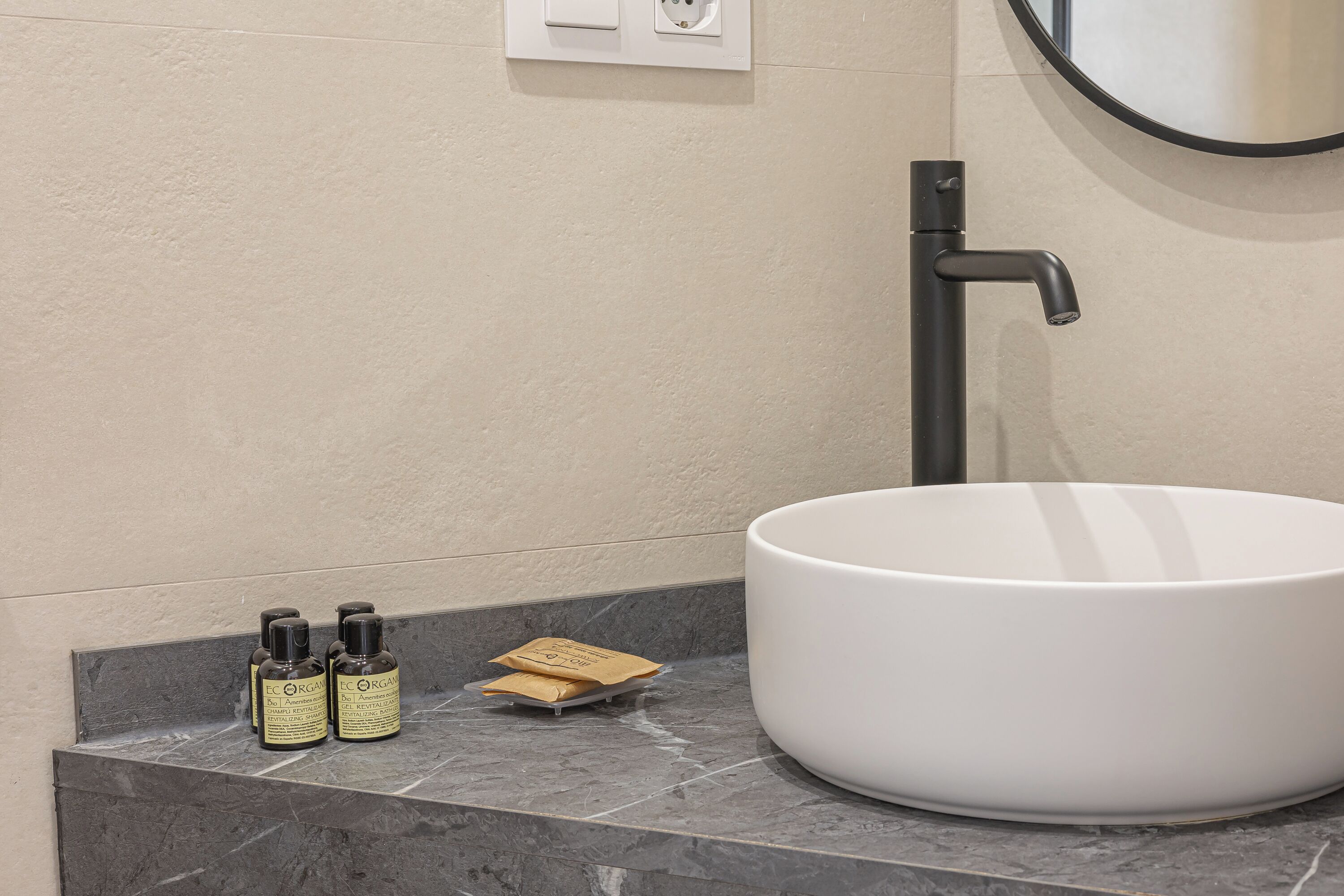 Un baño con un lavamanos grande de color blanco, un grifo negro y dos botellas de loción sobre una encimera de mármol.