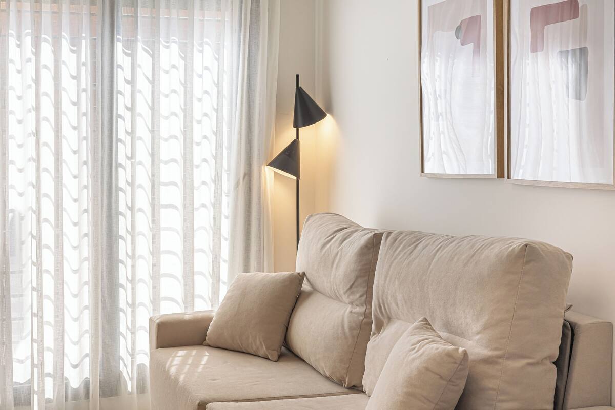A beige sofa with two cushions, a floor lamp, and abstract wall art.