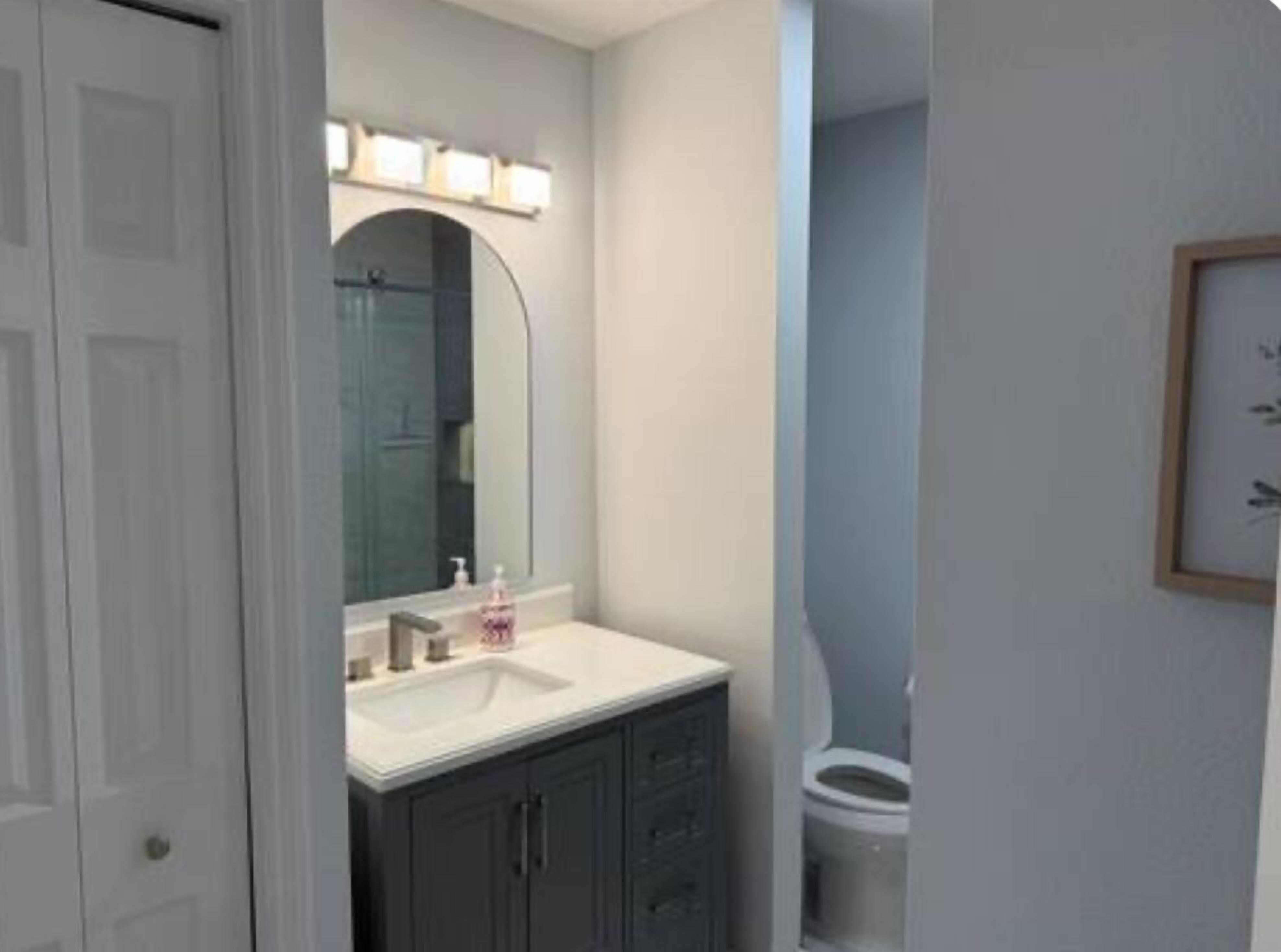 A bathroom with a white sink, dark cabinets, a mirror with lights, and a toilet.