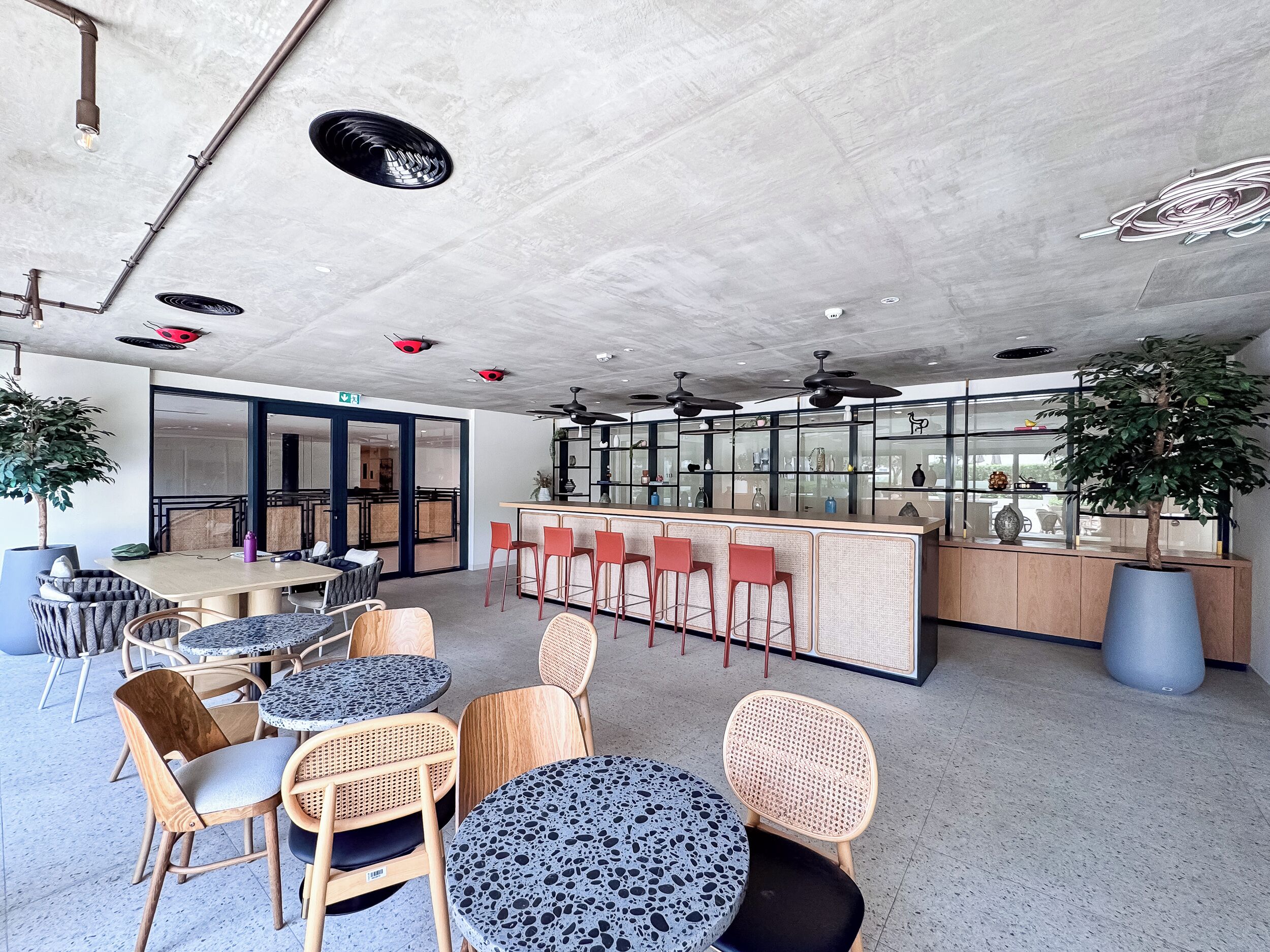 Um interior moderno com mesas redondas, cadeiras, área de bar e plantas em vasos.