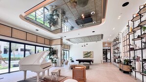 A spacious living room with a grand piano, a billiards table, and a high ceiling with skylights. - PVH - 2BR Golfville Dubai Hills (Dubai)