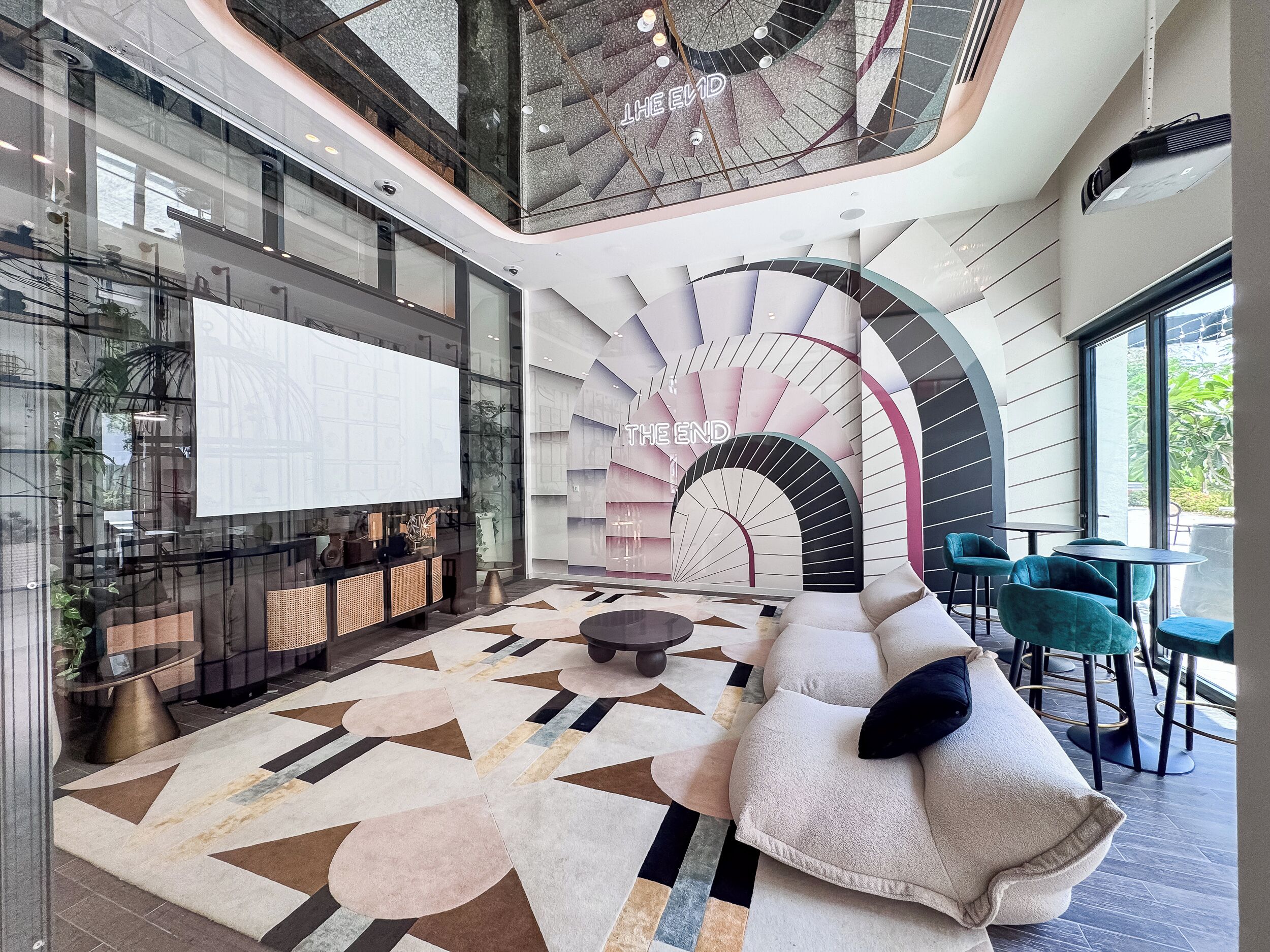 Un hall d’entrée spacieux doté d’un sol à motifs géométriques, d’un escalier moderne et d’un espace détente avec des fauteuils de couleur turquoise.