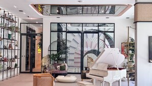 A spacious lobby with a grand piano, a wicker chair, and a variety of plants. - PVH - 2BR Golfville Dubai Hills (Dubai)