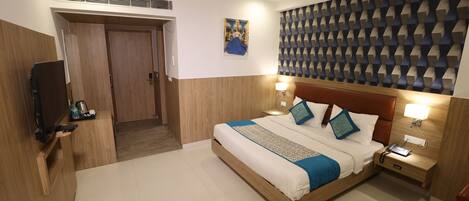 Habitación de hotel con cama de madera, televisor, mesita de noche y pared con diseño geométrico.