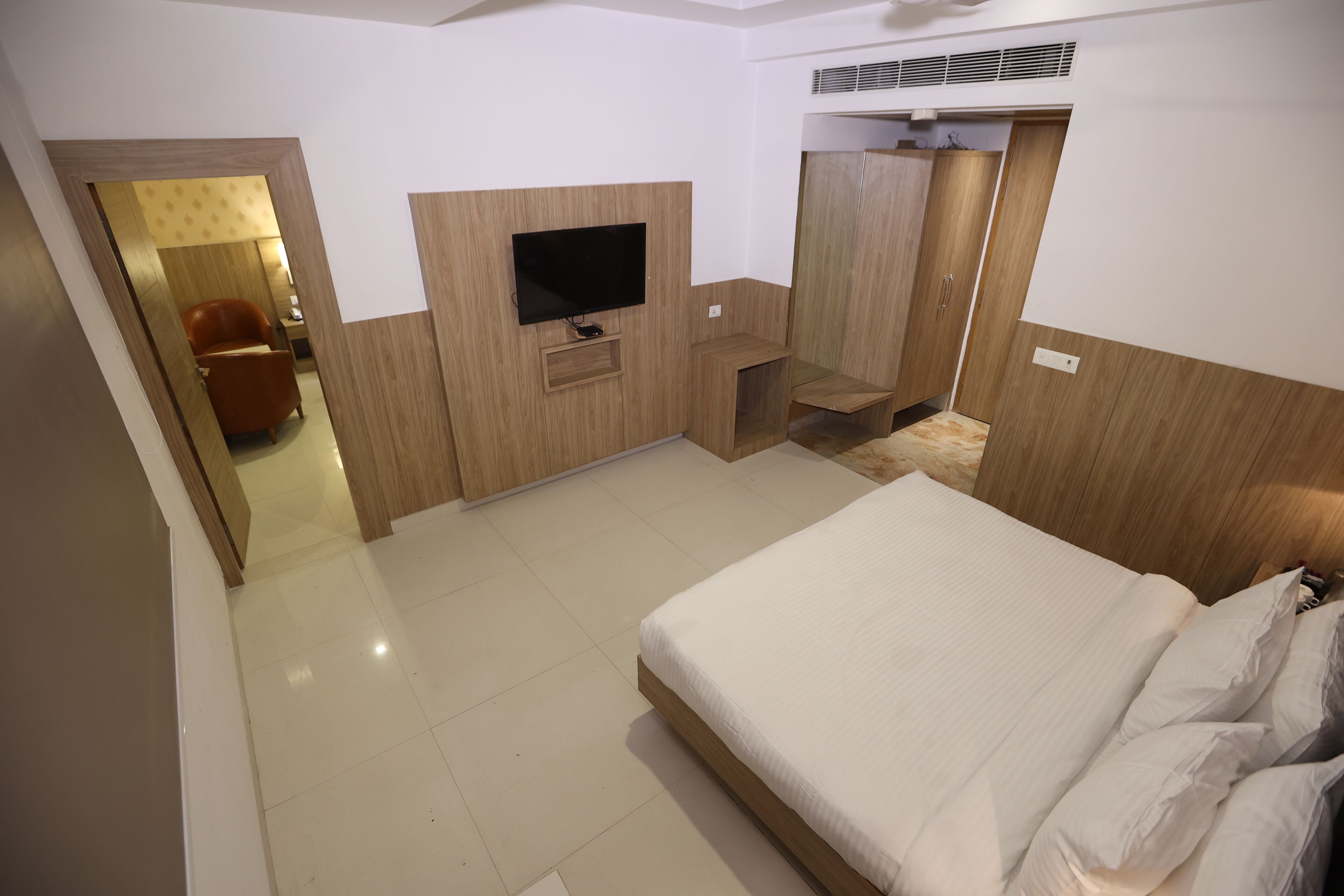 A hotel room with a bed, a TV, a wardrobe, and a seating area.