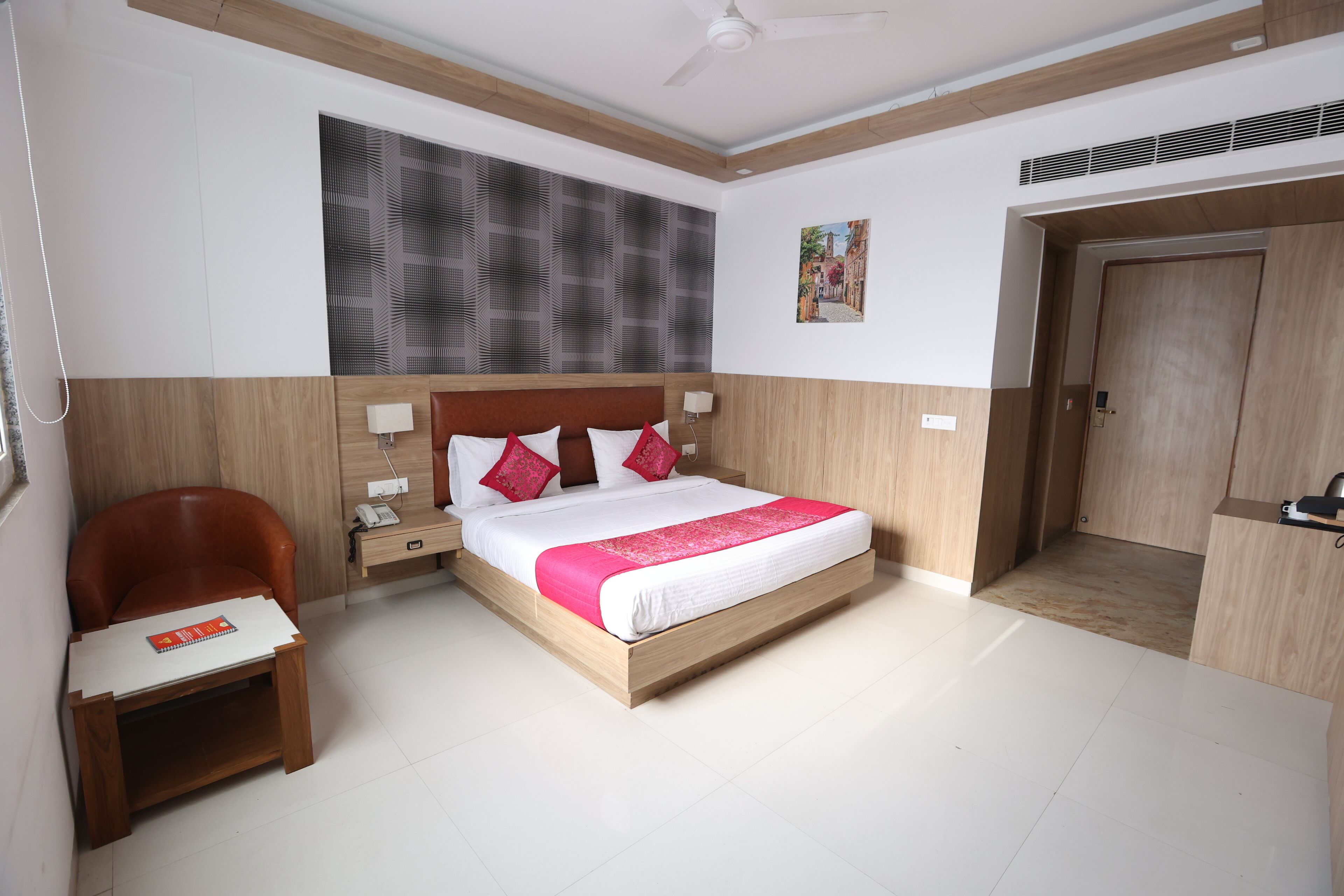 A modern hotel room with a wooden bed, a small desk, a chair, and a door.