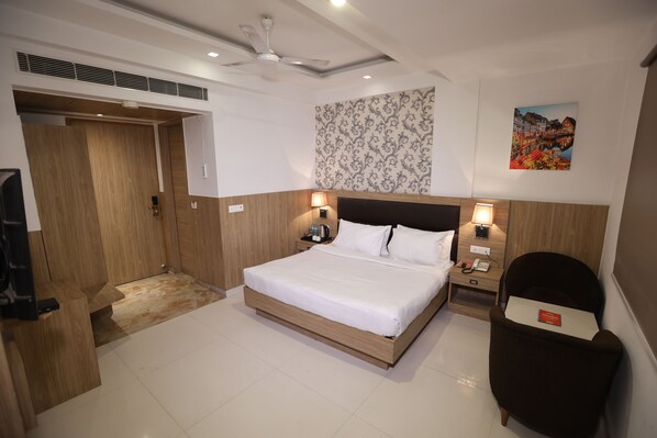 A modern hotel room with a large bed, wooden headboard, bedside lamps, a desk, and a chair. - The Elevate Hotel (New Delhi)