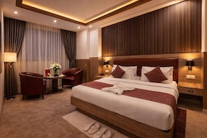 A hotel room with a large bed, a desk with a chair, a lamp, and a wall-mounted phone. - The Elevate Hotel (New Delhi)