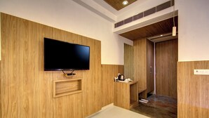 A modern room with a wooden wall, a mounted TV, a small shelf, and a door leading to another room. - The Elevate Hotel (New Delhi)
