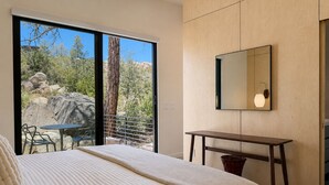 Ein Schlafzimmer mit einem großen Bett, einem Holztisch, einem Spiegel und Blick auf eine felsige Landschaft durch eine Glastür.