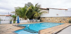 Una piscina rectangular con pared de piedra y solárium con baldosas.