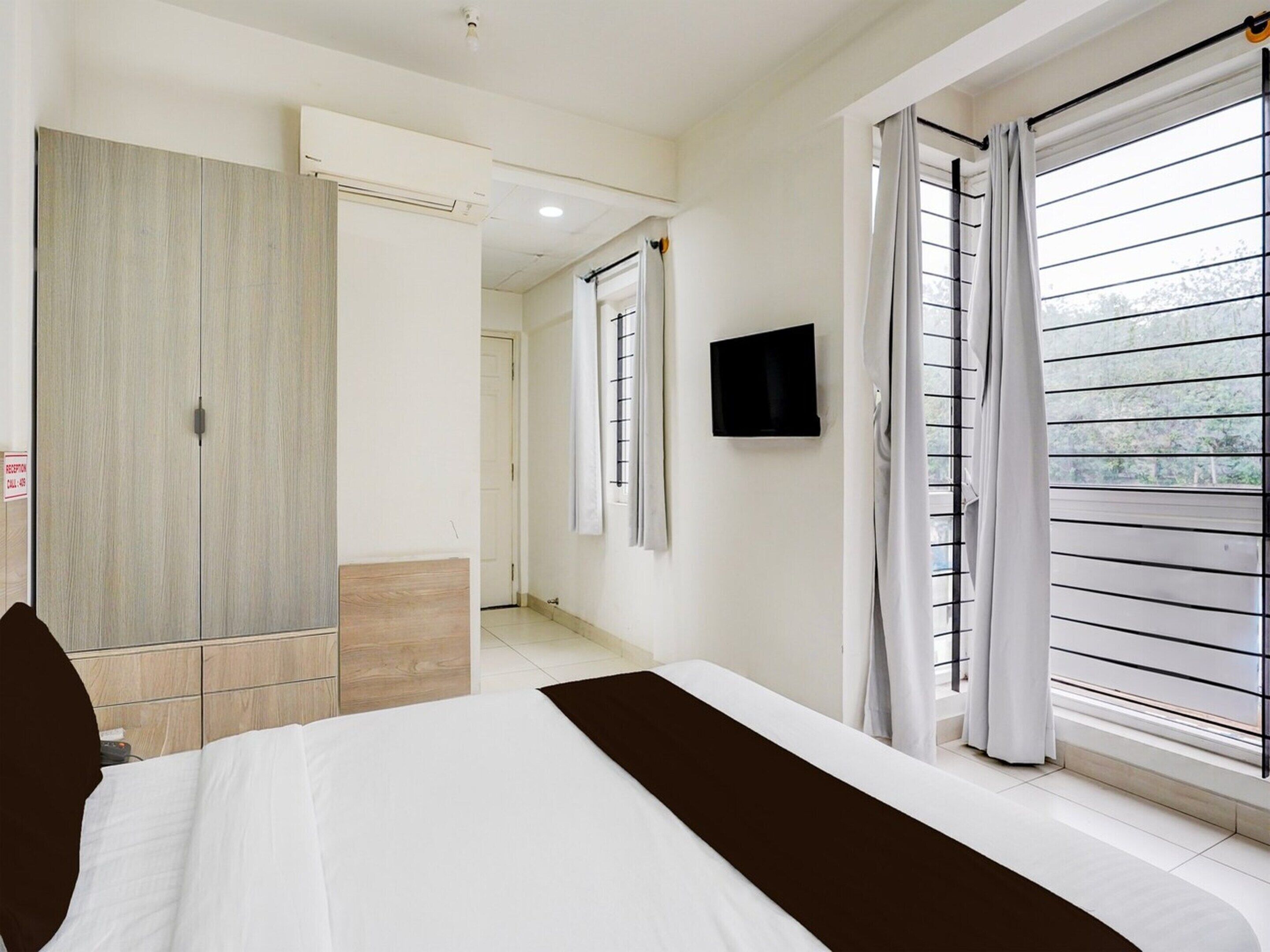 A hotel room with a bed, a TV, a wardrobe, and a window with curtains.