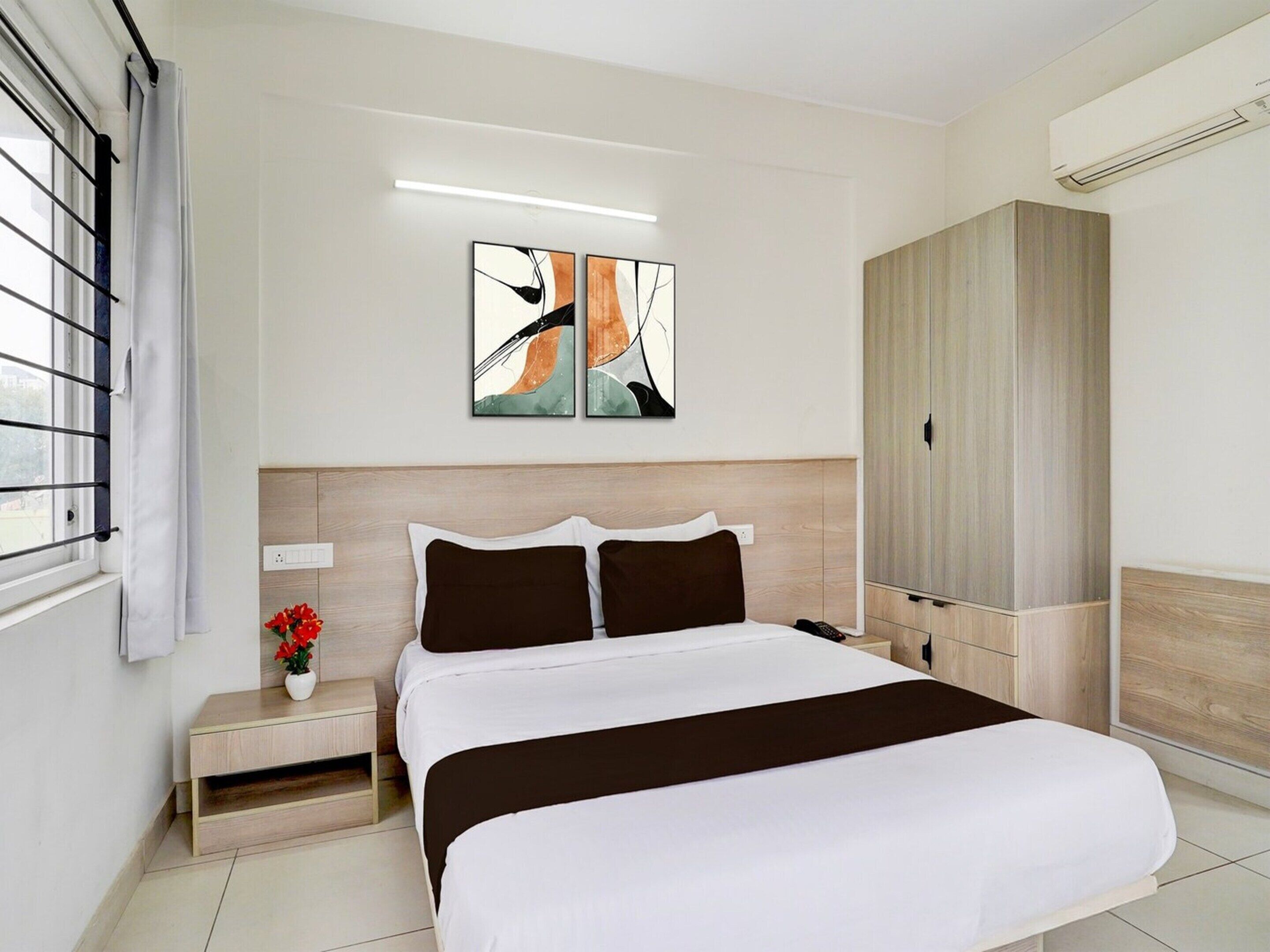 Une chambre d’hôtel comprenant un lit, une table de chevet, des œuvres d’art, une armoire et une fenêtre avec des stores.
