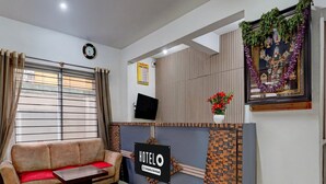 Uma área de recepção de hotel com um sofá, um balcão de recepção, um relógio, uma televisão e um painel decorativo.