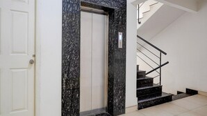 A modern elevator with a granite facade, a white door, and a staircase with black steps and metal railings. - Hotel O KSR Bengaluru City Junction (Bengaluru)