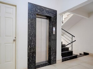 A modern elevator with a granite facade, a white door, and a staircase with black steps and metal railings. - Hotel O KSR Bengaluru City Junction (Bengaluru)