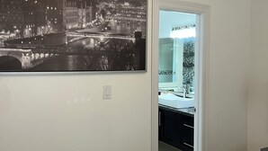 Ein Schlafzimmer mit einem großen schwarz-weiß Stadtbild, einer weißen Tür, die ins Badezimmer führt, und einem Bett mit weißer Bettdecke.