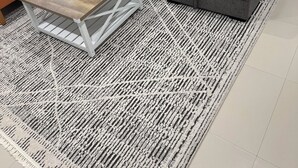 Ein Wohnzimmer mit grauem Sofa, orangefarbenen Kissen, einem Holztisch und einem gemusterten Teppich.
