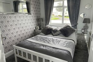 Une chambre à coucher comprenant un lit, une table de chevet, un miroir, une fenêtre avec des rideaux et une vue sur l’extérieur.