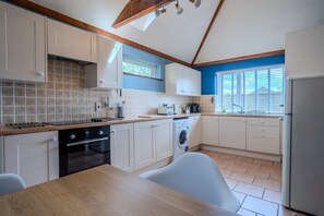 A modern kitchen with white cabinetry, a wooden countertop, a built-in oven, a washing machine, and a window with blinds.
