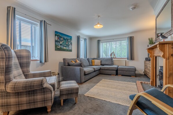 A cozy living room with a grey sectional sofa, plaid armchairs, and a small ottoman.