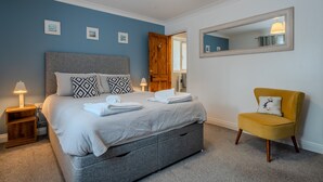 Un dormitorio con cama, mesita de noche, silla y espejo en la pared.