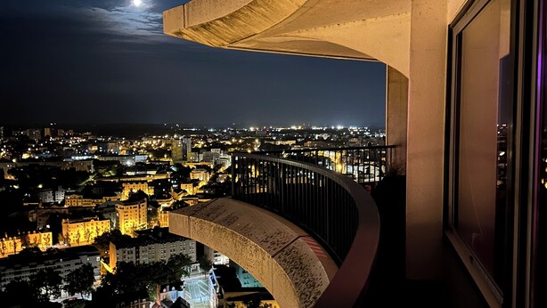 Panorama notturno di una città vista da un balcone con un elemento architettonico curvo.
