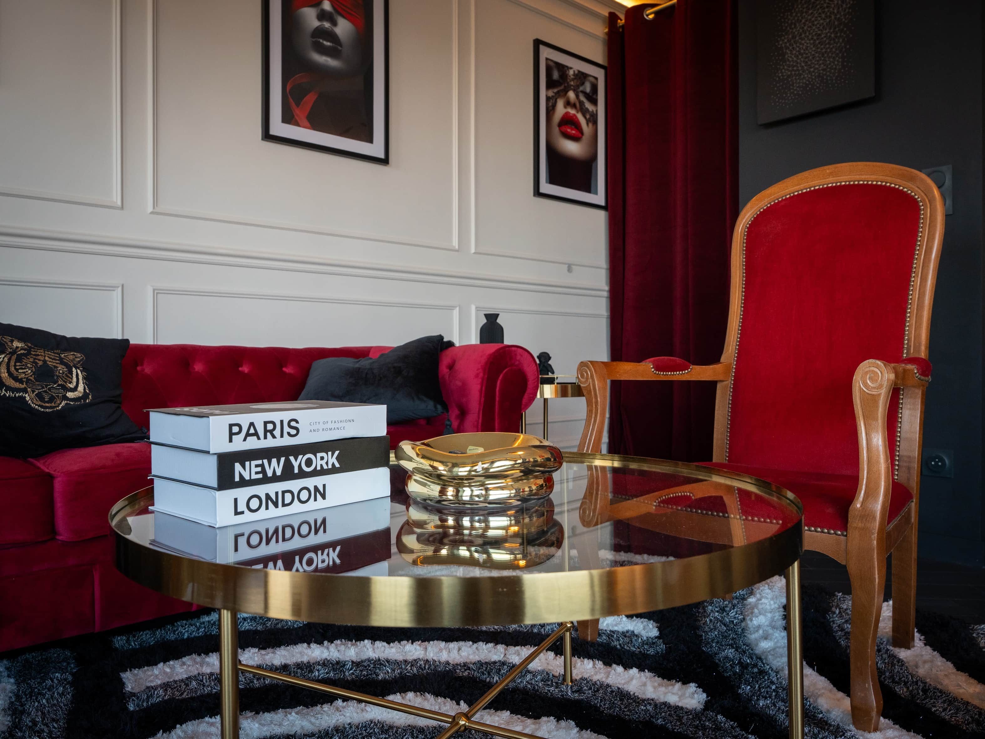 A room with a red velvet sofa, a glass coffee table with a book stack, and a red chair.
