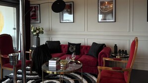 Un soggiorno moderno con un divano rosso, un tavolino rotondo e una poltrona rossa. Alle pareti si vedono quadri incorniciati, un vaso con fiori e un libro intitolato “PARIS”.