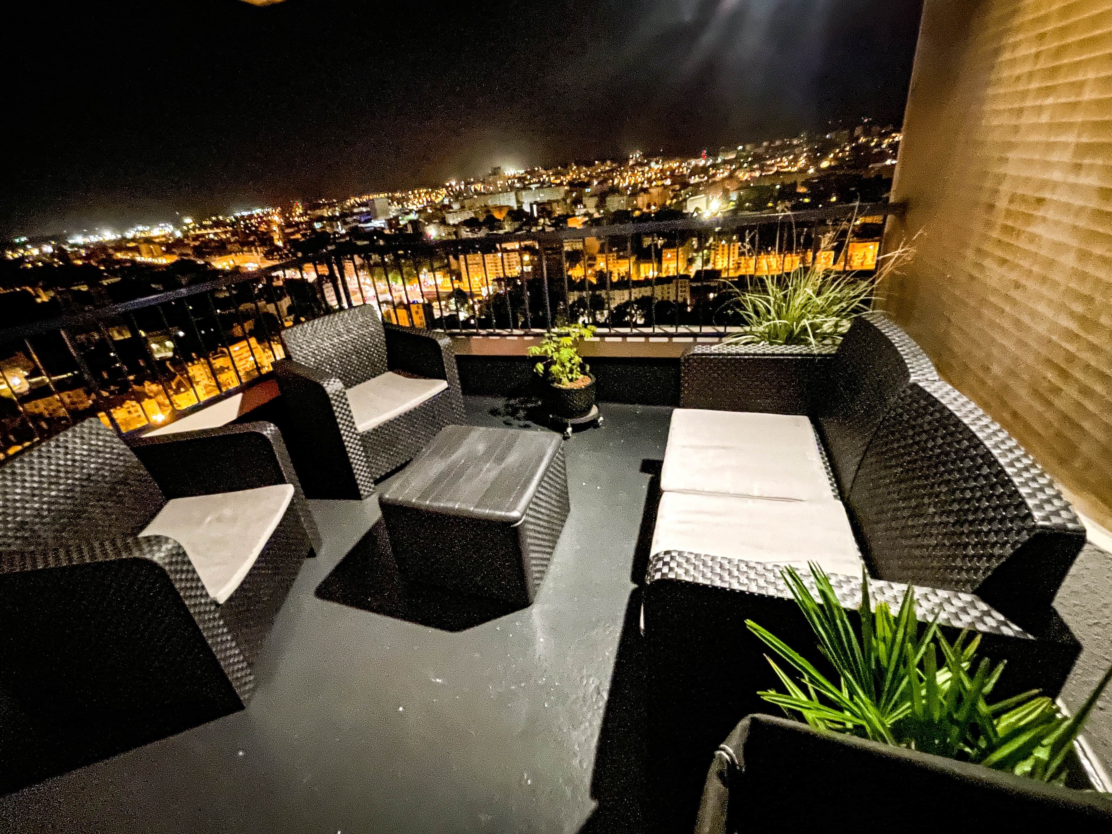 An outdoor seating area with wicker furniture and a view of a cityscape at night.