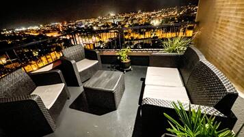 An outdoor seating area with wicker furniture and a view of a cityscape at night.
