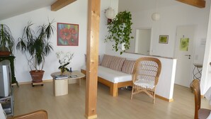 Una sala de estar con sofá, sillón de mimbre, una mesita de centro y plantas en macetas.