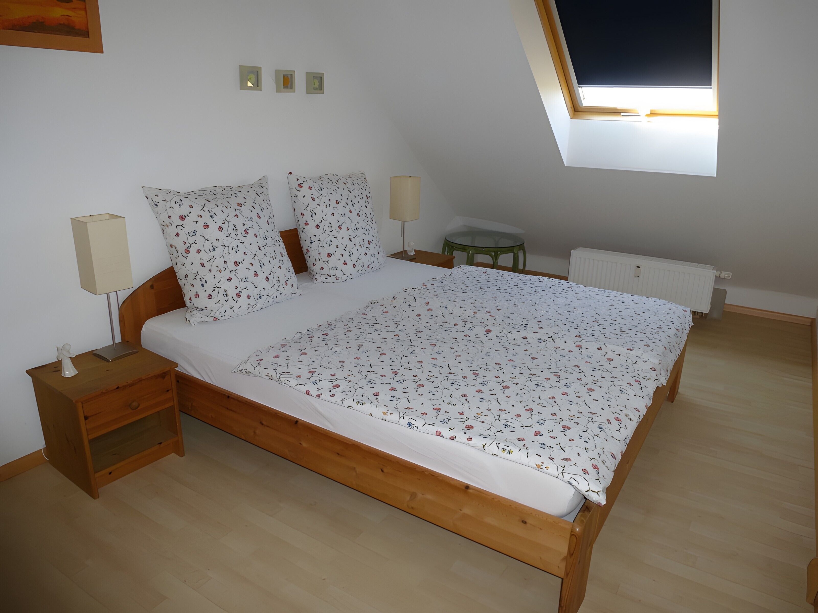 Une chambre à coucher avec un lit en bois, une table de chevet, une lampe, une petite table et un radiateur.