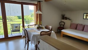 Una habitación con una mesa de comedor, sillas, un sofá, un radiador y vistas a zonas verdes a través de amplios ventanales.