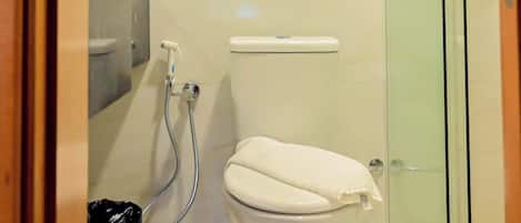 A bathroom with a toilet, a glass shower enclosure, and a trash bin.