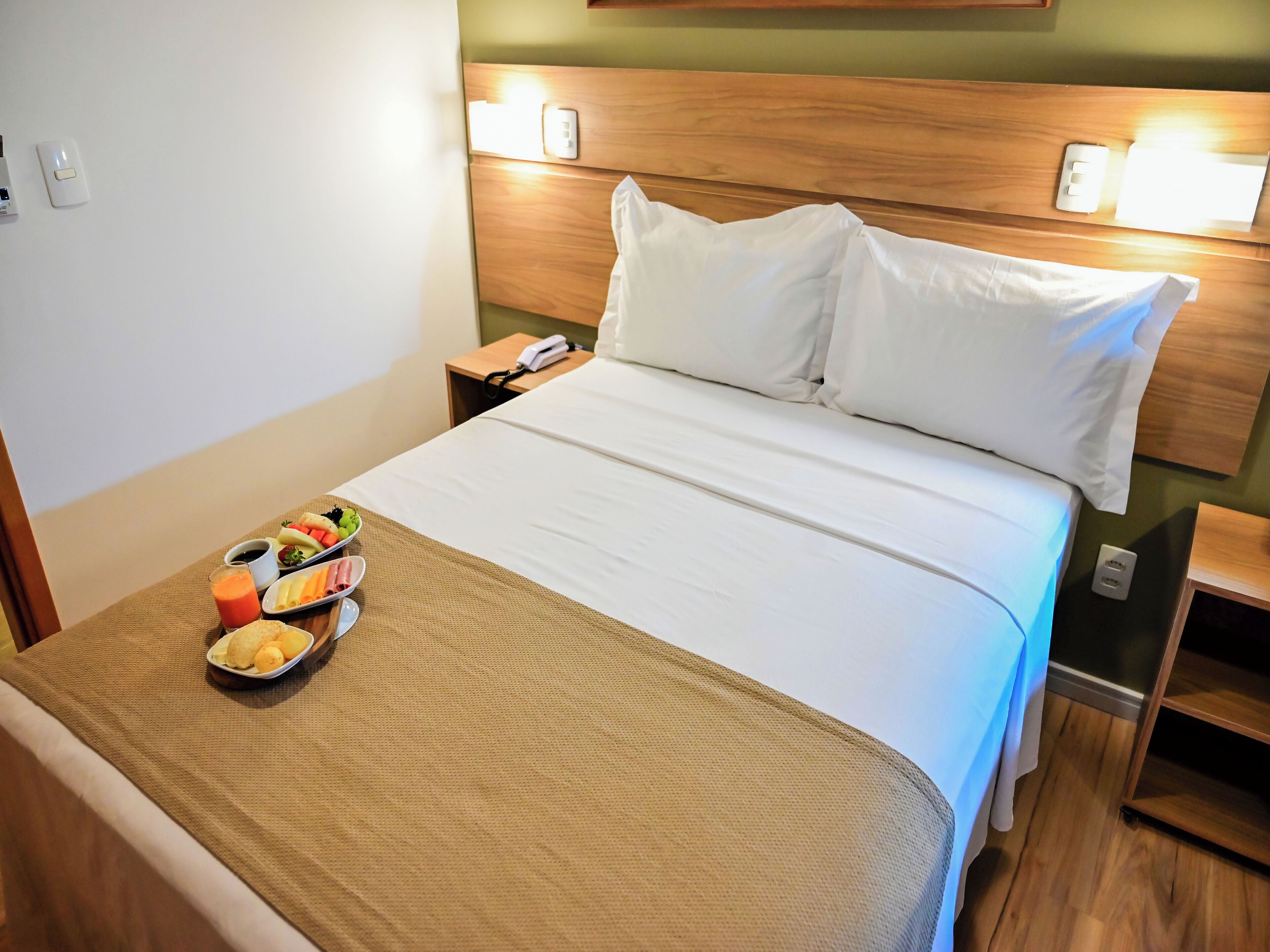 Siisti hotellihuone, jossa on huolitellusti pedattu sänky, yöpöytä, jossa on puhelin, ja aamiaistarjoilu sängyn päällä.