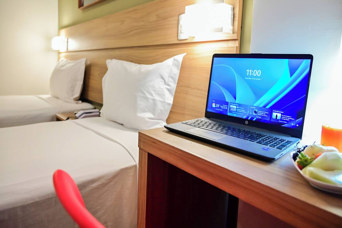 A hotel room with two beds, a laptop on a desk, and a plate of fruit.