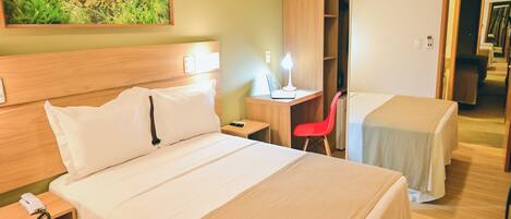 A hotel room with a large bed, a desk with a lamp, a red chair, and a wardrobe.